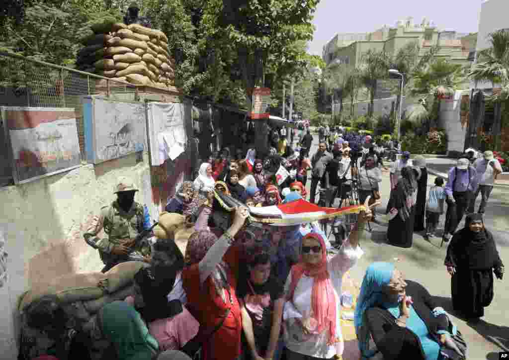 Voters line up as some take shade under a national flag outside a polling station to vote for president in Cairo, May 26, 2014.
