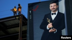 Công nhân xây dựng làm việc bên cạnh một tấm áp-phích với hình của người dẫn chương trình lễ trao giải Oscar lần thứ 90, Jimmy Kimmel, ở Hollywood, Los Angeles, bang California, ngày 1 tháng 3, 2018. 