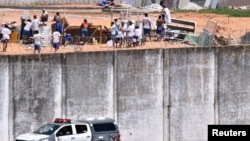 A police car drives past the wall of Alcacuz prison while inmates from different gangs, left and right, protect themselves during an uprising, in Natal, Rio Grande do Norte state, Brazil, Jan. 17, 2017.