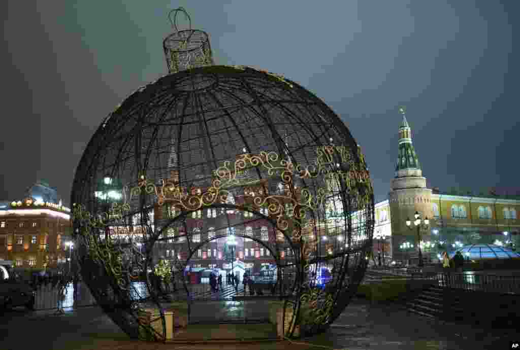 People walk behind the fence of the Christmas sphere erected at the Manezhnaya Square, just outside the Kremlin, in Moscow, Russia. Organizers claim 9.5-meter (31 feet) high sphere is the biggest in the world.