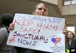 Protester Jennifer Smith-Camejo holds a sign during an anti-Trump and anti-Gimenez rally in downtown Miami, Jan. 31, 2017. Miami-Dade County Mayor Carlos Gimenez had issued a controversial order assuring the Trump administration that Miami-Dade was not functioning as a sanctuary city for illegal immigrants.