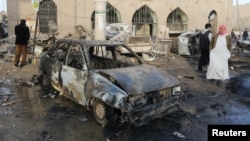 People walk past the wreckage of a car outside Raqqa Museum, after what activists said were airstrikes by forces loyal to Syria's President Bashar al-Assad in Raqqa, eastern Syria, Nov. 25, 2014.