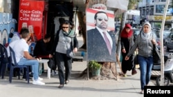 People walk next to a poster depicting Lebanon's Prime Minister Saad al-Hariri, who has resigned from his post, along a street in the mainly Sunni Beirut neighborhood of Tariq al-Jadideh in Beirut, Lebanon, Nov. 6, 2017.