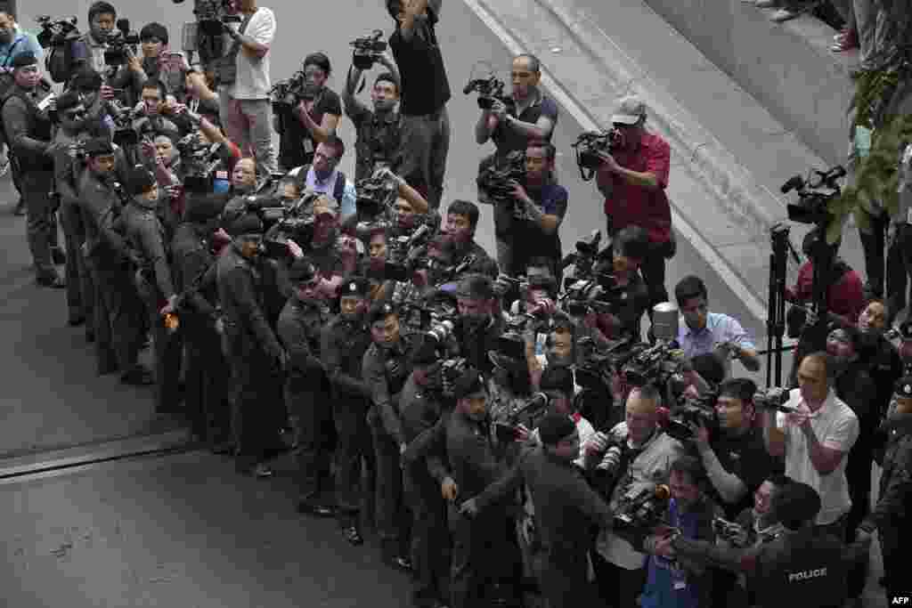 The media stand behind a line of police officers as a foreign suspect in the August 17 Erawan shrine bombing, identified by the ruling junta as Yusufu Mieraili (not pictured), gets out of a police van during a reenactment with police officers nearby the Erawan shrine (not pictured) in Bangkok, Thailand.