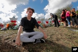 Chris Grady, a student at Marjory Stoneman Douglas High School, sits by a memorial outside the school, for Wednesday's mass shooting, in Parkland, Fla., Monday, Feb. 19, 2018.