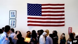 FILE - People file past the U.S. flag and a portrait of President Barack Obama on their way to attend a naturalization ceremony in Irving, Texas. 