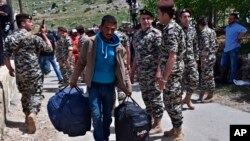 FILE - In this April, 18, 2018 photo, a Syrian displaced man, who fled the war in Syria, carries his belongings past Lebanese General Security soldiers, as he prepares to return to his village of Beit Jinn in Syria, near the Lebanese-Syrian border, in Sh