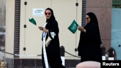 Saudi women hold national flags as they walk on a street during Saudi National Day in Riyadh, Saudi Arabia, Sept. 23, 2016. 