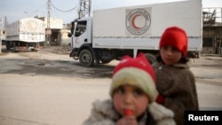 FILE - Children stand along a street as an aid convoy of the Syrian Arab Red Crescent and United Nations drives through the rebel-held besieged city of Douma, on the outskirts of Damascus, Syria, Feb. 23, 2016.