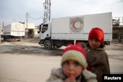 Children stand along a street as an aid convoy of Syrian Arab Red Crescent and United Nation (UN) drives through the rebel held besieged city of Douma towards the besieged town of Kafr Batna to deliver aid, on the outskirts of Damascus, Syria, Feb. 23, 2016.