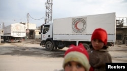 Children stand along a street as an aid convoy of Syrian Arab Red Crescent and United Nation (UN) drives through the rebel held besieged city of Douma towards the besieged town of Kafr Batna to deliver aid, on the outskirts of Damascus, Syria, Feb. 23, 2016.