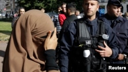 A woman wearing a full-face veil, or niqab, covers her eyes as she stands near police in Lille, France, in this September 22, 2012, file photo.
