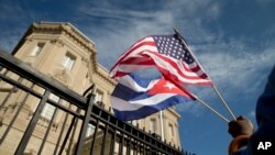 A Cuban American, holds a U.S. and a Cuban flag as he stands outside the new Cuban embassy in Washington, July 20, 2015. With President-elect Donald Trump assuming power in January, the future of the warming of relations between the two countries, initiated by President Barack Obama, is now in question.