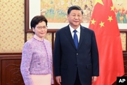 In this photo released by Xinhua News Agency, Chinese President Xi Jinping, right, poses for a photo with Chief Executive of the Hong Kong Special Administrative Region Carrie Lam, during their meeting in Beijing, China, Dec. 22, 2021.