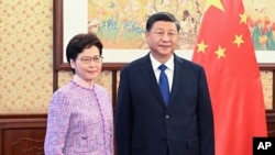 In this photo released by Xinhua News Agency, Chinese President Xi Jinping, right, poses for a photo with Chief Executive of the Hong Kong Special Administrative Region Carrie Lam, during their meeting in Beijing, China, Dec. 22, 2021. 