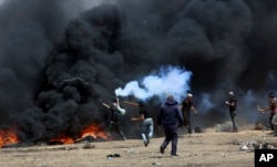 FILE - A Palestinian protester throws back a tear gas canister at Israeli soldiers as others burn tires near the Israeli fence during a protest at the Gaza Strip's border with Israel, May 11, 2018.