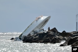 Investigators look at a boat overturned on a jetty, Sunday, Sept. 25, 2016, off Miami Beach, Florida.