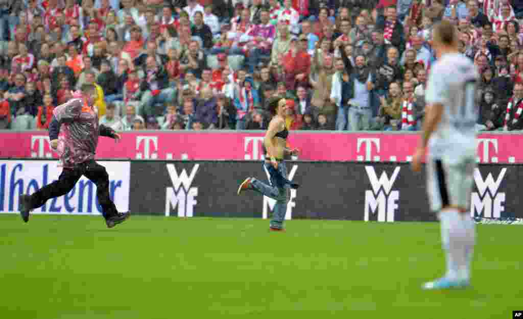 Một nh&acirc;n vi&ecirc;n an ninh rượt theo một phụ nữ kh&ocirc;ng mặc &aacute;o ngo&agrave;i tr&ecirc;n s&acirc;n cỏ trong trận b&oacute;ng đ&aacute; giữa hai đội FC Bayern Munich v&agrave; FC Freiburg tại Munich, Đức.