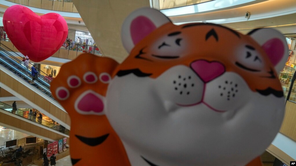 A cartoon tiger is displayed as shoppers wearing face masks to help protect fro the coronavirus ride on escalators at a mall during the Lunar New Year Eve in Beijing, Monday, Jan. 31, 2022. (AP Photo/Andy Wong)