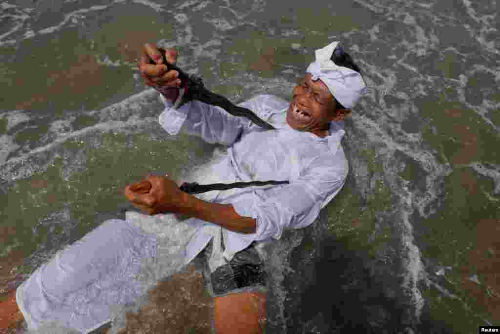 A Balinese Hindu worshiper attempts to stab himself with traditional Kris daggers while in trance during Melasti, a purification ceremony ahead of the holy day of Nyepi on a beach in Gianyar, Bali, Indonesia.