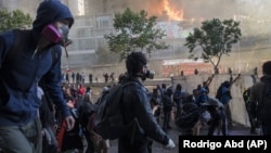 Protesters walk toward police as firefighters work to put out a fire set by protesters at a shopping center in Santiago, Chile, Monday, Oct. 28, 2019.