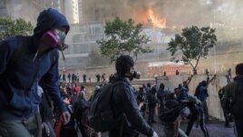 Protesters walk toward police as firefighters work to put out a fire set by protesters at a shopping center in Santiago, Chile, Monday, Oct. 28, 2019.