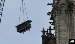 A crane hoists scaffolding past gargoyles outside the Notre Dame Cathedral in Paris, April 18, 2019.