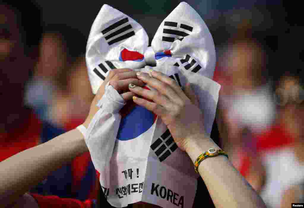 A soccer fan covers her face with a banner of a South Korean national flag while watching a live television broadcast after their team was defeated by Belgium in their 2014 World Cup Group H soccer match, in Seoul, June 27, 2014.