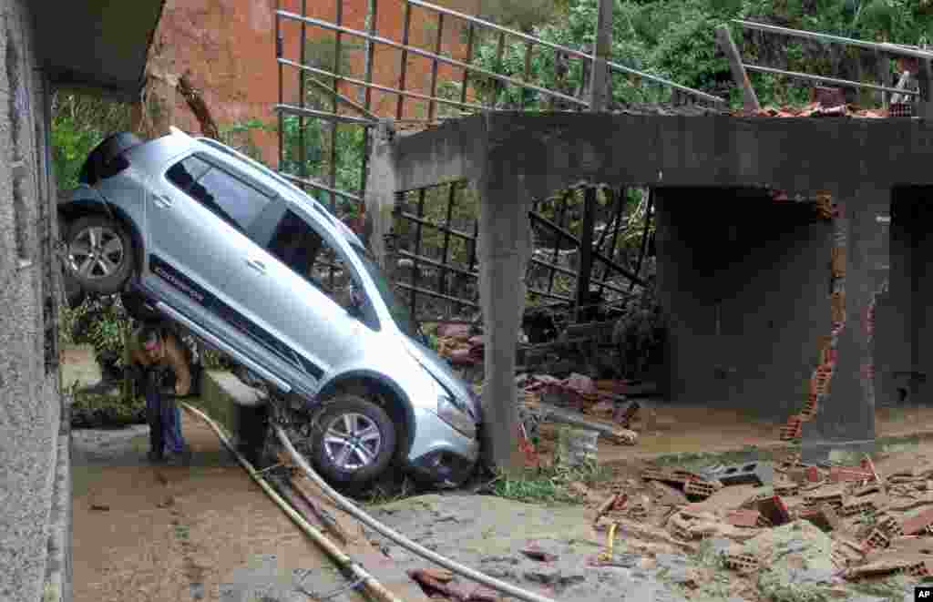 Um homem passa sob um carro danificado pelas enxurradas e deslizamentos em Teresópolis.