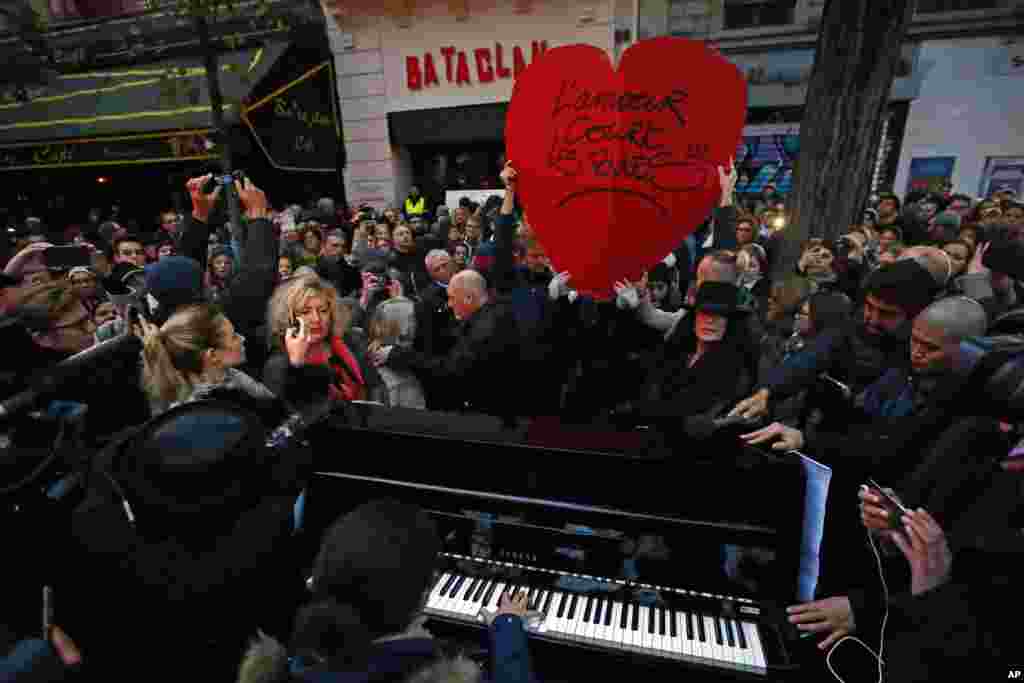 Seorang perempuan bermain piano, dekat tanda jantung hati besar bertuliskan "Cinta ada di jalan" di depan gedung konser Bataclan di Paris, Perancis (13/11), setelah upacara untuk mengenang para korban serangan maut di Paris tahun lalu yang menewaskan 130 orang. (AP/Francois Mori)