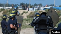 French riot police stand guard at the entrance to "the Jungle" as dozens of migrants try to storm trucks that are heading toward the ferry terminal in Calais, France, Sept. 21, 2016.