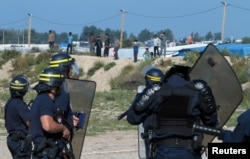 FILE - French riot police stand guard at the entrance to the "Jungle" as dozens of migrants try to storm trucks that are heading toward the ferry terminal in Calais, France, Sept. 21, 2016.