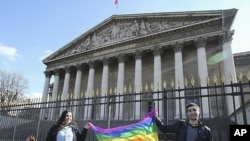 Pro gay marriage activists celebrate outside the National Assembly, background, with a banner symbolizing the gay movement after French lawmakers legalized same-sex marriage, Tuesday, April 23, 2013 in Paris. Lawmakers legalized same-sex marriage after mo