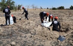 This Sunday, July 14, 2019 frame grab from video, shows Syrian workers of the Civil Council of Raqqa removing human remains at the site of a mass grave believed to contain the bodies of civilians and Islamic State militants, in Raqqa.