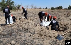 This Sunday, July 14, 2019 frame grab from video, shows Syrian workers of the Civil Council of Raqqa removing human remains at the site of a mass grave believed to contain the bodies of civilians and Islamic State militants, in Raqqa.