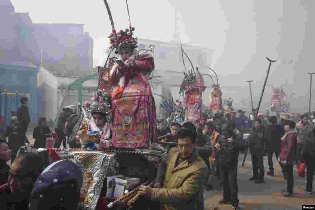 Children wearing costumes play with their mobile phones as they perform in a &quot;Taigeqiao&quot; parade, in Yiwu, Zhejiang province, China.