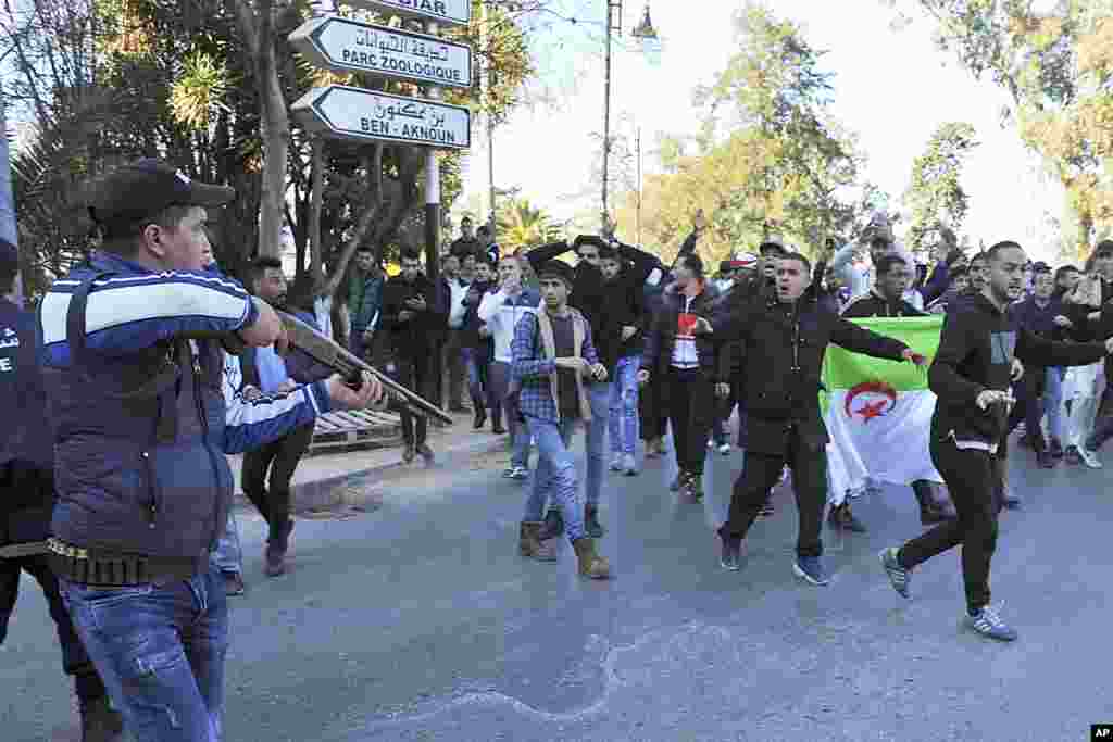 A police officer holds his gun as protesters, carrying their national flag, march in the streets of the Algerian capital, Algiers, to denounce President Abdelaziz Bouteflika's bid for a fifth term.