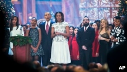 The first family, from left; Malia Obama, Sasha Obama, President Barack Obama, and first lady Michelle Obama, join, fifth from left to rright; AJ McLean of the Backstreet Boys, country singer Sheryl Crow, and Janelle Monáe, Dec. 15, 2013.