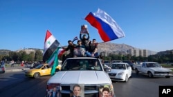 FILE - Syrian government supporters wave Syrian, Iranian and Russian flags during demonstrations following April 2018 military strikes by U.S., British and French forces in Syria. Russia and Iran are allies of Syrian President Bashar al-Assad.