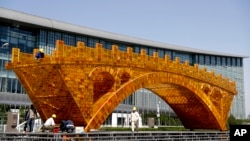 FILE - Workers install wires on a Golden Bridge of Silk Road structure outside the National Convention Center, the venue for the Belt and Road Forum for International Cooperation, in Beijing, April 18, 2017.