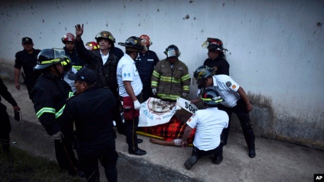 Los bomberos rodean el cuerpo de un hombre dentro de un reformatorio para jóvenes y hombres durante un disturbio en el Centro Correccional Etapa II en San José Pinula, Guatemala, el domingo 19 de marzo de 2017.