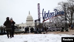 La gente se reúne junto a un cartel: 'Los votantes deciden, protegen la democracia', antes de una vigilia con velas en el primer aniversario del asalto al Capitolio, en las afueras del Legislativo de los EE. UU. el 6 de enero de 2022.