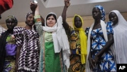 Aktivis Pakistan Malala Yousafzai, mengangkat tangan beberapa siswi di Chibok yang lolos dari penculikan dalam konferensi pers di Abuja, Nigeria, Senin (14/7).