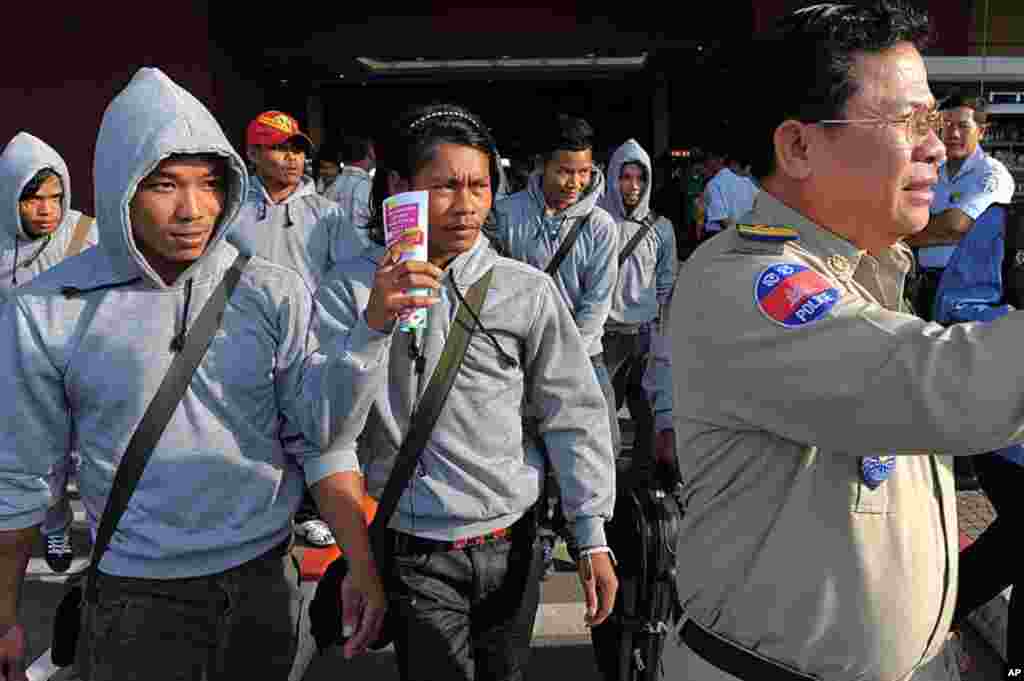 A Cambodian policeman (R) escorts thirty trafficked fishermen returning from Indonesia after being freed or escaping from slave-like conditions on Thai fishing vessels at the Phnom Penh International airport on December 12, 2011. (AFP)