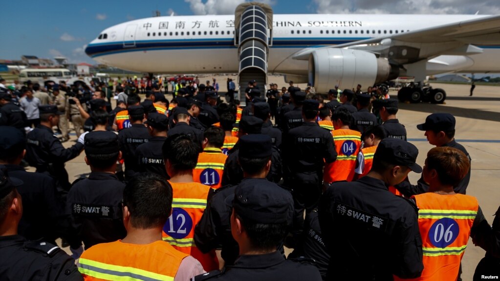 Các công dân Trung Quốc bị tình nghi lừa đảo tống tiền qua mạng (áo khoác da cam) được cảnh sát Trung Quốc áp tải chờ lên máy bay tại Sân bay Quốc tế Phnom Penh, ở Phnom Penh, Campuchia, ngày 12 tháng 10, 2017.