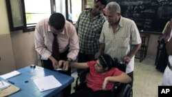 An Egyptian election worker helps a disabled woman in a wheelchair to vote at a polling station during the second day of the presidential runoff in Cairo, June 17, 2012.