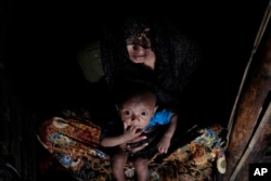 Mohsena Begum, a Rohingya who escaped to Bangladesh from Myanmar, holds her child and sits at the entrance of a room of an unregistered refugee camp in Teknaf, near Cox's Bazar, a southern coastal district south of Dhaka, Bangladesh, Dec. 2, 2016.