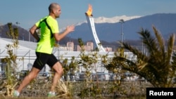 A man jogs on a sunny day as the Olympic Cauldron and flame are seen in the background in the Olympic Park during the 2014 Winter Olympic Games, Feb. 12, 2014.