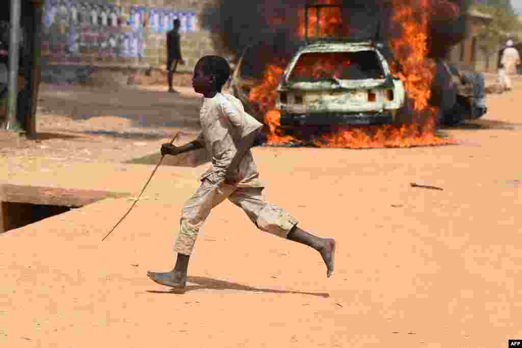 A boy runs past burning cars following deadly clashes between supporters of the ruling All Progressives Congress (APC) and the opposition Peoples Democratic Party (PDP) in Kano, Nigeria.