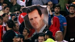 FILE - Syrian soccer fans hold a poster of their president, Bashar al-Assad, before a match with Iran, at Azadi Stadium in Tehran, Iran, Sept. 5, 2017.
